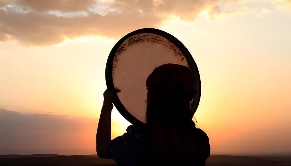 يک زن رو به غروب آفتاب در حال نواختن دف